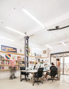 two people sitting at desks in an open area with bookshelves and shelves