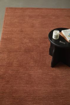 a coffee table with a book and candle on it in front of a rug that is red