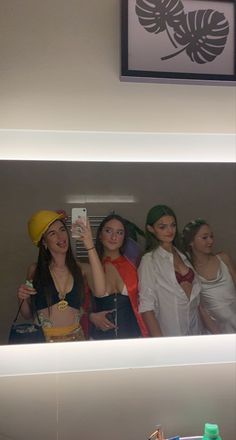 four women are taking a selfie in the mirror with their cell phones and one is wearing a yellow hard hat