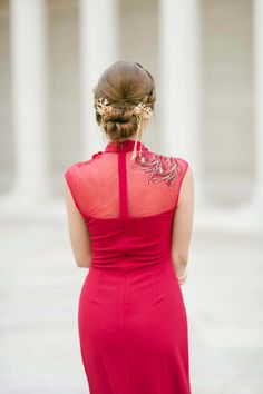 a woman in a red dress is looking down at the ground with columns behind her