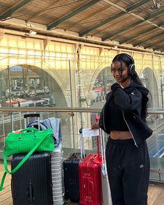 a woman standing next to luggage in front of a train station window with headphones on