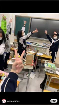 two girls and one boy wearing masks in a classroom with their hands up to the ceiling