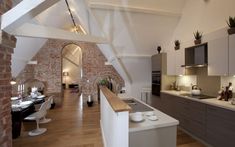 an open kitchen and dining room area with exposed brick walls, hardwood flooring and white countertops