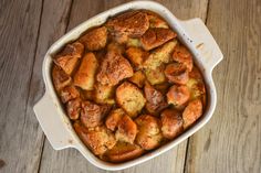 a casserole dish filled with bread and cinnamon buns on a wooden table