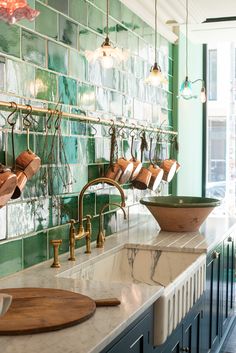 two sinks in a green tiled bathroom with copper faucets and hanging lights above them