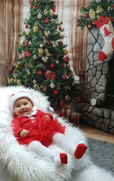 a baby sitting in a white chair next to a christmas tree and a fire place