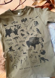 Handprinted Tshirts on Cotton with Ecofriendly and water-based inks. Drawn, Printed and Sewn by Chantel Traub this print features many of the Animals or Plants at Risk in Alberta, Canada.  This work celebrates the beauty of the creatures who live close to home and brings awareness to our ecosystem's fragility.  printed on heavyweight 100% cotton in unisex sizes For free pickup in Calgary please enter coupon code LOCALPICKUP *Disclaimer: the status of species is often changing, this is not a comp Nature T-shirt, Job Clothes, Graphic Shirt Design, Animal Graphic Tee, Adventure Outfit, Outdoor Fashion, Versatile Outfits, Mens Trends, Quirky Design