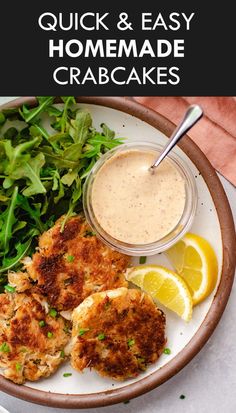 crab cakes on a plate with lemon wedges and greens next to a bowl of sauce