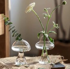 two clear vases with flowers in them sitting on a burlap table cloth