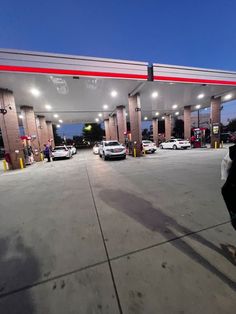 a person riding a skateboard in front of a gas station with cars parked nearby