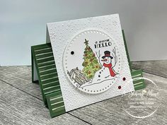 a card with a snowman and a christmas tree on it, sitting on a wooden table