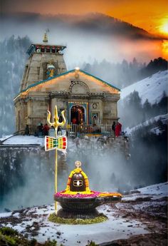 a small temple in the middle of a mountain with snow on the ground and people standing around it