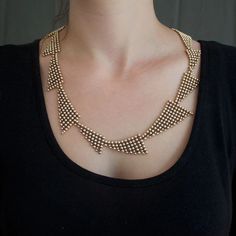 a woman wearing a black shirt and a gold necklace on her neck, with beads in the shape of squares