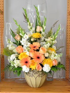 a vase filled with lots of flowers on top of a wooden shelf next to wine glasses