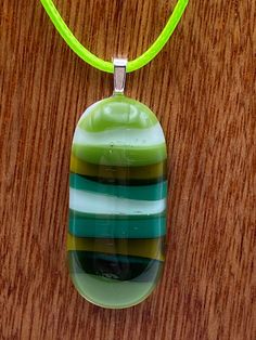 DragonFusedGlass are proud to sell this green stripes design fused glass necklace and matching earring set. We have used shades of green glass and fused them on to a clear glass background to create this hand crafted this absolutely beautiful tactile pendant This utterly unique pendant is supplied on a 45cm green coloured cord and comes in its own presentation box. Due to the kiln firing process, every creation is unique and therefore no two items created will ever be totally the same.  The photographs displayed here are of the actual finished product for sale, so that what you see is the unique item you will own.  Thank you for viewing and please do look at our other creations in our Etsy Shop: https://dragonfusedglass.etsy.com Handmade Modern Green Jewelry, Green Handmade Modern Jewelry, Modern Handmade Green Jewelry, Modern Green Handmade Jewelry, Adjustable Green Recycled Glass Necklace, Green Glass Pendant Jewelry, Unique Green Glass Necklaces, Unique Green Glass Necklace, Green Recycled Glass Pendant Jewelry