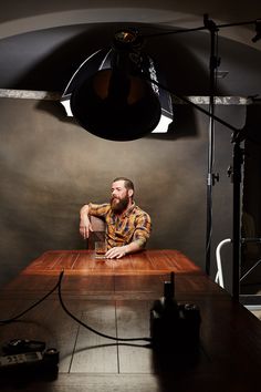 a man sitting at a table with a glass in front of him and lighting behind him