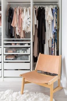 a white closet filled with lots of clothes and other items on shelves next to a chair