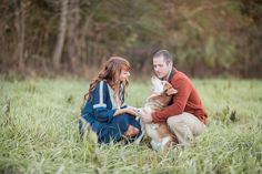 a man and woman are sitting in the grass with their dog, who is looking at each other