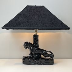 a table lamp with a black shade on it's base and a cat figurine underneath