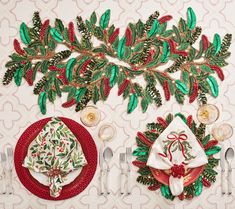 the table is set for christmas dinner with red and green place mats, silverware, and napkins