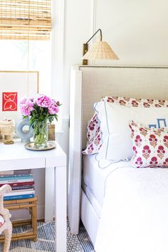 a white bed sitting next to a table with flowers on top of it and a vase filled with pink flowers