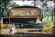 a black and white dog sitting in front of a food truck with a chalkboard sign