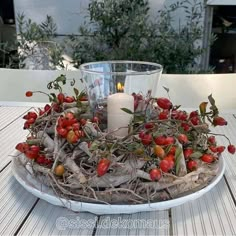 a candle sits on top of a plate with branches and berries