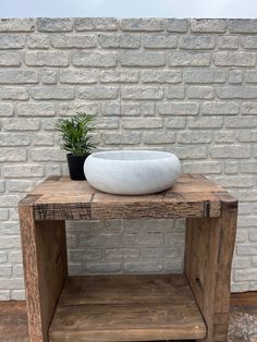 a white bowl sitting on top of a wooden table next to a brick wall and potted plant