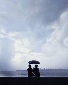 two people sitting under an umbrella near the ocean