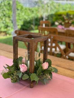 a candle holder with flowers and greenery sits on a pink table cloth in front of an outdoor dining area