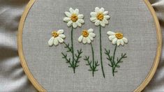 three white daisies on a gray background in a wooden hoop