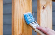 a person holding a paintbrush in their hand near a wooden fence with wood slats