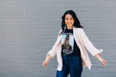 a woman standing in front of a brick wall wearing jeans and a t - shirt