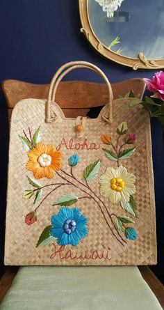 "Totes adorable: Oversized vintage souvenir purse makes the perfect summer beach bag. A friendly \"Aloha, Hawaii\" message graces the front, woven through bright, winding hibiscus flowers. Loop and wooden button closure. Structured body and handles stand on their own, making a gorgeous display piece when not in use. Use it for toting market finds, beach towels or holding dried flowers! Dimensions Height: 17.5 inches Width: 15.25 inches Side depth: 4 inches (with give) Handles at tallest point: 6 Embroidered Rectangular Straw Bag For Beach, Green Embroidered Beach Bags, Handmade Rectangular Beach Bag, Handmade Beachy Rectangular Beach Bag, Beachy Handmade Rectangular Beach Bag, Blue Tropical Rectangular Bag, Tropical Blue Rectangular Bag, Embroidered Rectangular Straw Bag For Vacation, Retro Handmade Shoulder Bag For Beach