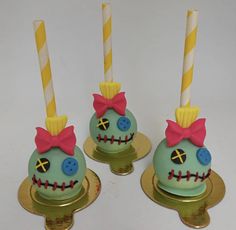 three decorated cake pops with candles in the shape of skulls and faces on gold plates