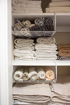 an organized closet filled with folded towels and folded linens in white bins on shelves