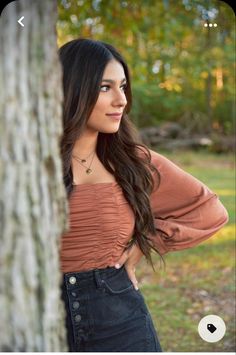 a beautiful young woman standing next to a tree