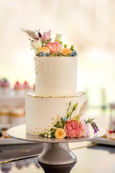 a three tiered cake with flowers and feathers on the top is sitting on a table