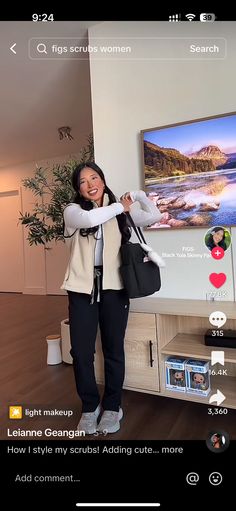 a woman standing in front of a flat screen tv holding a black bag and smiling