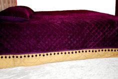 a bed with a purple comforter on top of it next to a red headboard