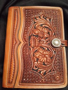 a brown leather journal with floral designs on the front and sides, sitting on a black cloth