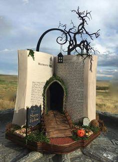 an open book sculpture sitting on top of a rock covered in grass and vines with a tree growing out of it