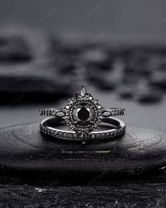 a black and white photo of an engagement ring on top of a stone slab with other rings in the background