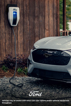 an electric car plugged in to a charger next to a wooden fence and building