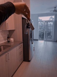 a person is holding keys in front of a refrigerator and looking at the kitchen door