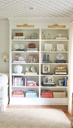 a living room filled with lots of white furniture and bookshelves on top of each other