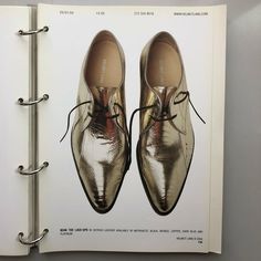 an open book with a pair of gold shoes on top of the page, in front of a white background