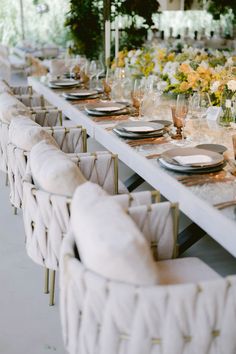 a long table set with white chairs and place settings for an elegant dinner party setting