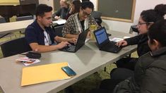 four people sitting at a table with laptops