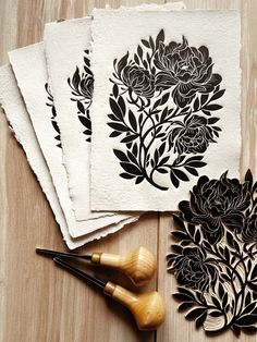 four black and white paper cut outs with flowers on them next to some ink pens